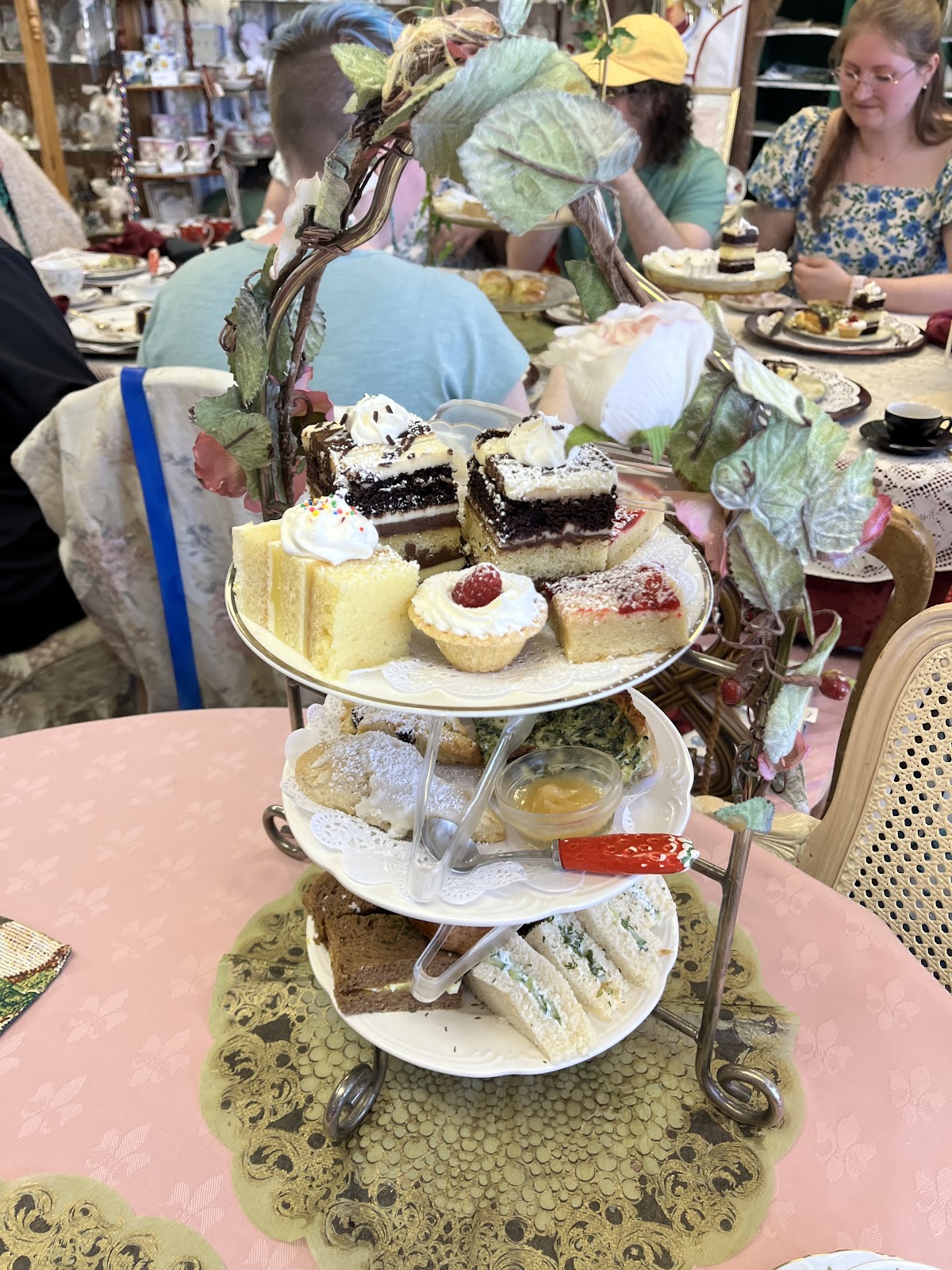 A tiered tea stand with guests dining in the busy tea room behind