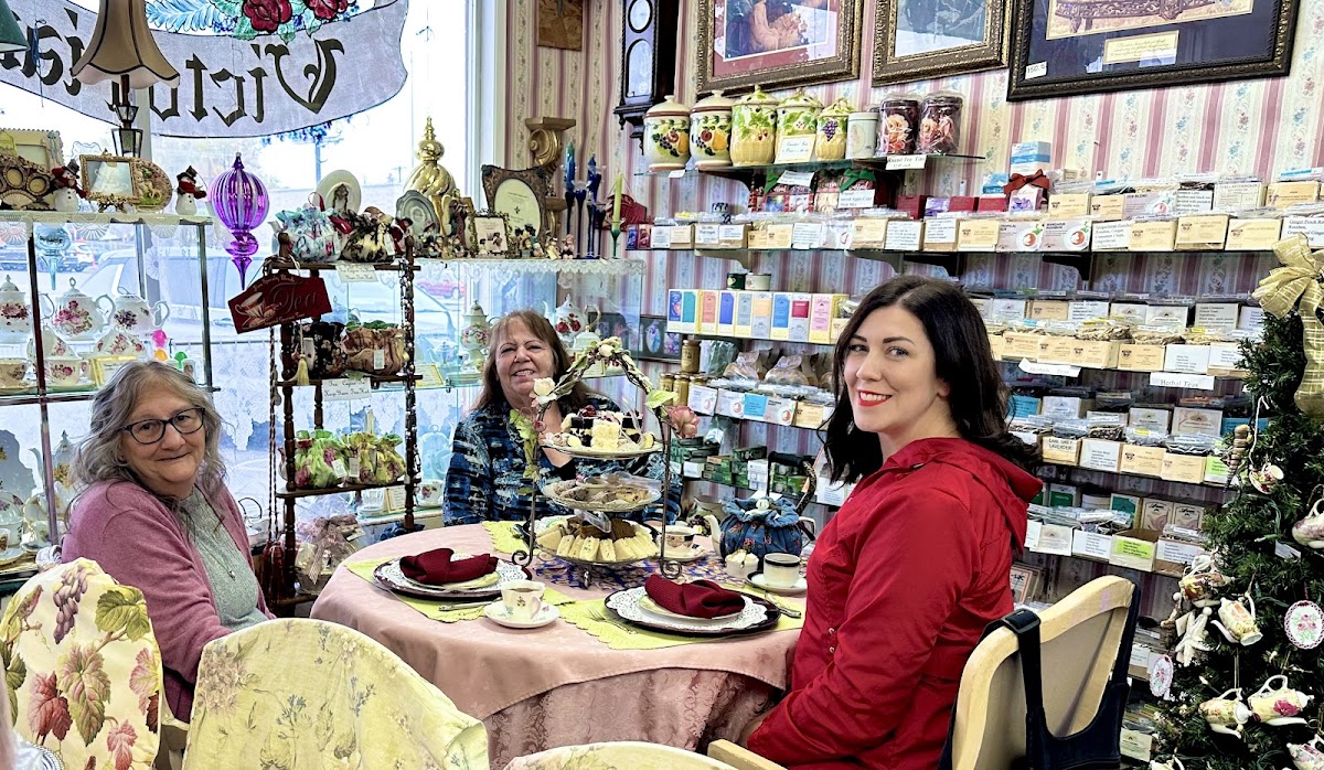 Guests smiling at a tea table inside Victorian Connection, the tea wall behind them