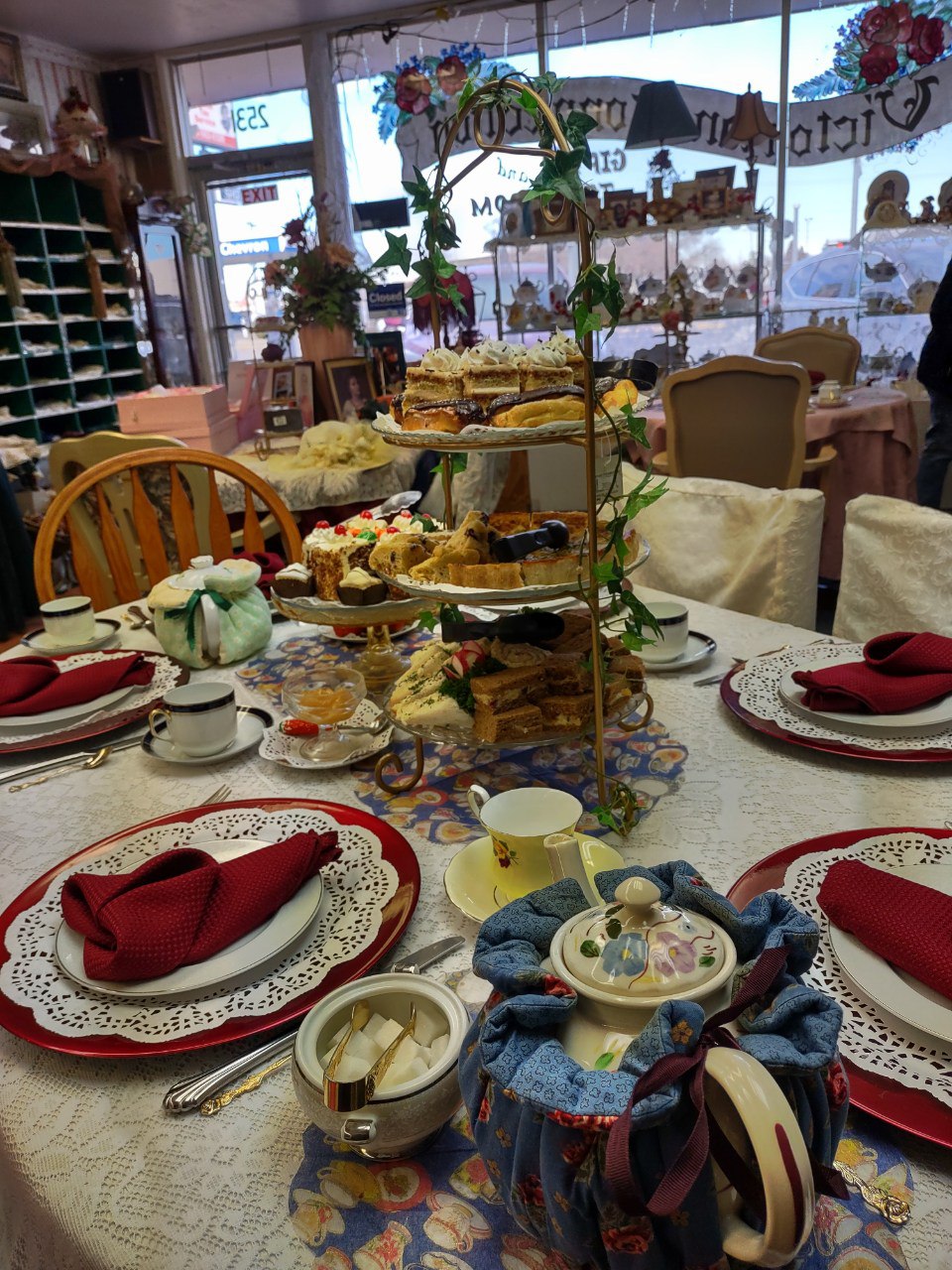 A full Victorian tea table setting with burgundy napkins and the storefront window beyond
