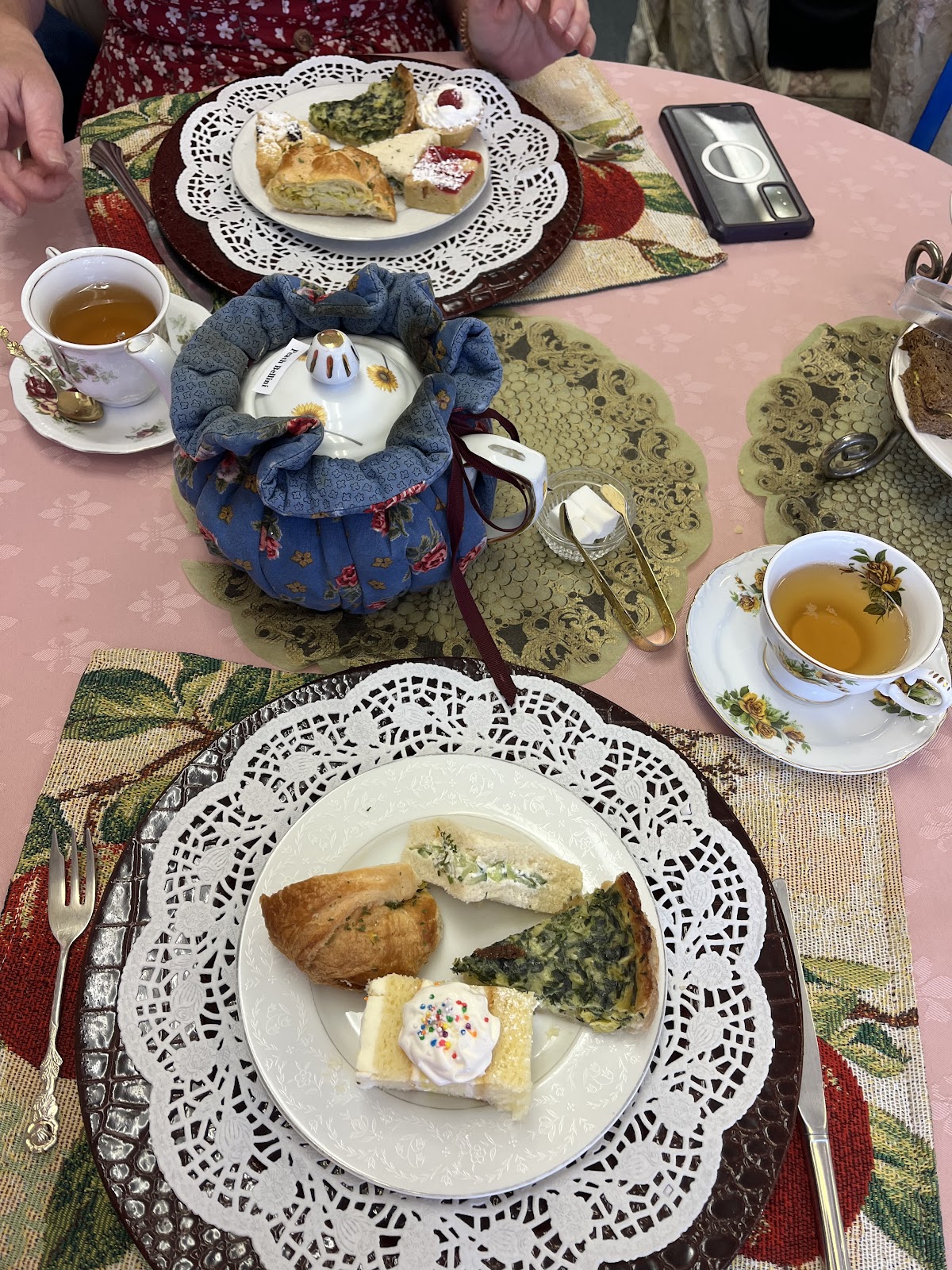 Tea cups with a tea cozy, quiche and scones on lace doilies