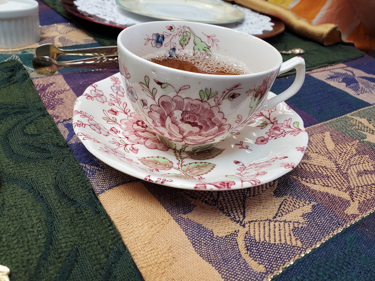 A rose-patterned china teacup of tea on a tapestry placemat
